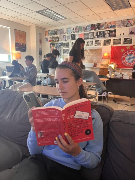 A teenager escapes the horrors of the world by scrolling through her phone, the notorious "iGen" by Jean Twenge in hand.